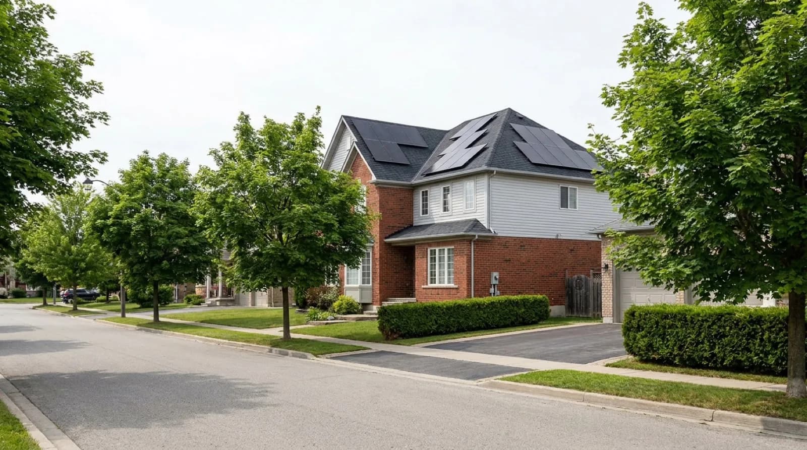 A two-storey detached house in a Toronto suburb on a clear day, its south-facing asphalt shingle roof partly covered by a rack-mounted solar array, mature maples in leaf along the street